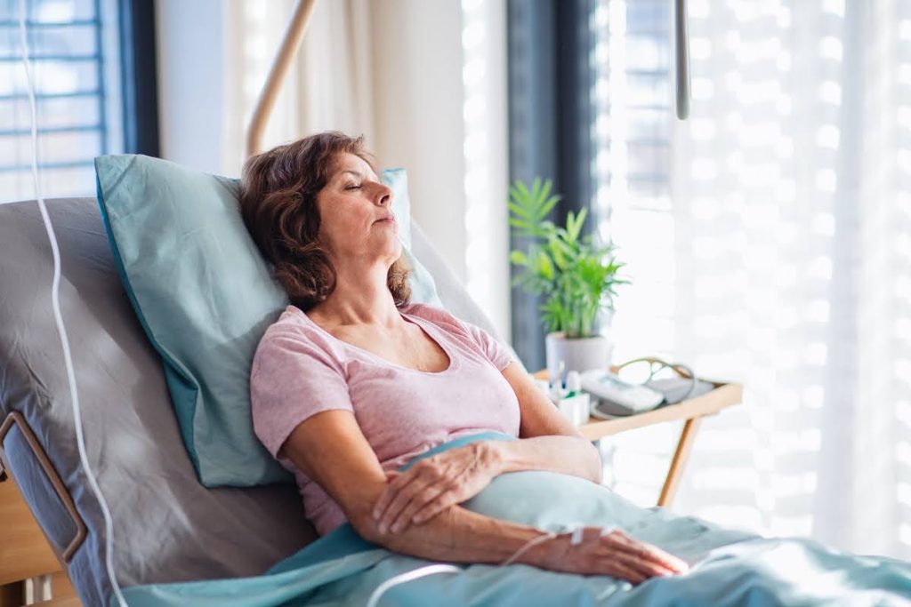 A female patient with IV drip lying in bed in hospital room, sleeping.